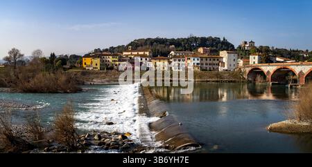 Une vue pittoresque d'une petite ville italienne au bord d'une rivière, avec des bâtiments colorés, un pont de pierre et une cascade. La scène est placée contre un clair Banque D'Images
