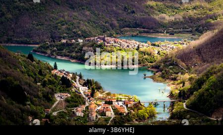 Vue aérienne d'un village pittoresque niché entre des collines verdoyantes et un lac serein. Le paysage présente des rivières sinueuses, une verdure vibrante, et Banque D'Images