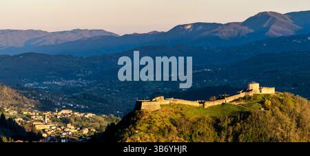 Une vue panoramique sur un château historique perché sur une colline, entouré de montagnes verdoyantes et de vallées. Le soleil couchant projette une lueur chaude sur le Banque D'Images