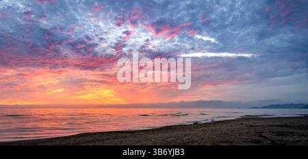 Une scène de plage sereine au coucher du soleil, avec des couleurs vibrantes dans le ciel avec des nuages reflétant les nuances d'orange, rose et violet. La mer calme reflète th Banque D'Images