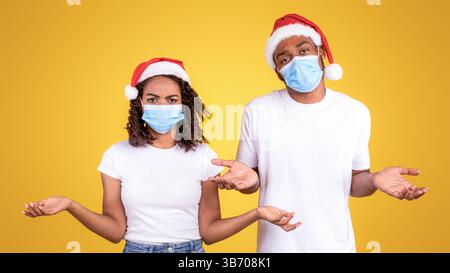 Couple noir portant des masques coronavirus et des chapeaux de Noël, fond jaune Banque D'Images