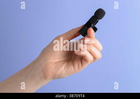 Femme tenant le micro-cravate sur fond bleu clair, gros plan Banque D'Images