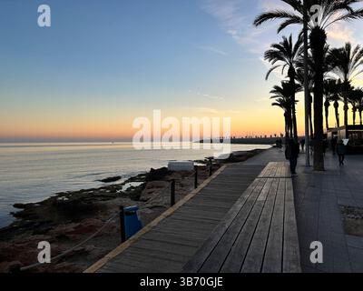 Profitez d'une vue paisible sur le coucher du soleil tout en marchant le long d'une promenade balnéaire bordée de beaux palmiers Banque D'Images