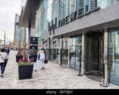 Le puits, Toronto, Canada. Entrée de bâtiment moderne à usage mixte avec façade en verre, portes tournantes et vue sur la rue avec les gens marchant. Banque D'Images