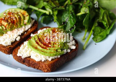 Toast de seigle avec fromage cottage, avocat, sésame, graines de lin, paprika fumé et poivre. Servi avec épinards frais, jus de citron, huile d'olive et balsamique Banque D'Images