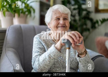 Femme âgée reposant ses mains sur une canne tout en étant assise dans un fauteuil Banque D'Images