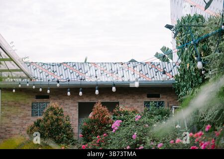 Jardin confortable avec guirlande lumineuse festive et motif batik traditionnel. Un cadre extérieur animé avec des fleurs et des plantes encadrant le bâtiment. Banque D'Images