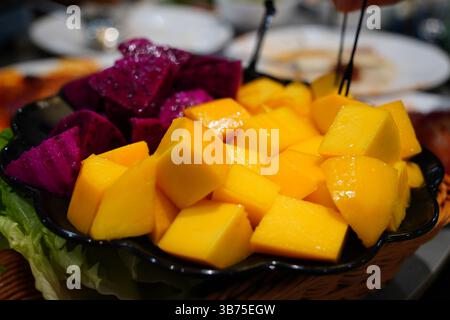 Gros plan de mangue fraîche en cubes et de fruits du dragon sur une assiette sombre – plateau de fruits tropicaux Banque D'Images