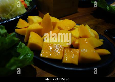 Gros plan de mangue fraîche en cubes et de fruits du dragon sur une assiette sombre – plateau de fruits tropicaux Banque D'Images
