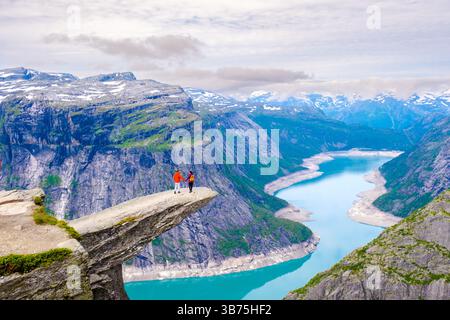 Deux aventuriers se tiennent sur la formation rocheuse emblématique de Trolltunga, en Norvège, en admirant une vue imprenable sur le Lysefjord en contrebas. Banque D'Images
