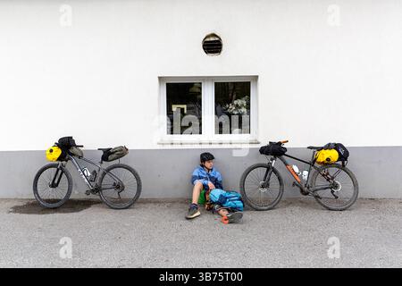 Touriste sur un voyage de vélo, bikepacking de Ljubljana à Piran en Slovénie, se détendre sur un trottoir dans une petite ville de vrhnika Banque D'Images