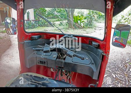 Commandes de direction et tableau de bord d'un tuk tuk rouge dans un village tropical sans personne visible pendant la journée Banque D'Images