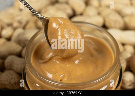 Beurre de cacahuètes crémeux en cuillère et cacahuètes crues. Banque D'Images