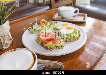 Un délicieux petit déjeuner à tartiner présente du pain grillé garni d'avocat crémeux, des tranches de saumon fumé, des tomates cerises et un œuf dur. ACCO Banque D'Images