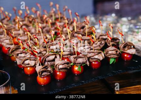 Petits canapés de bœuf élégants servis sur des tomates cerises accompagnées de légumes verts, brochés pour une présentation élégante lors d'événements ou d'une restauration. Banque D'Images