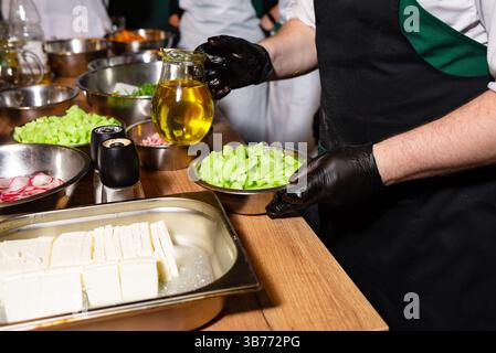 Divers légumes fraîchement hachés et fromage feta préparés dans des bols, avec un pichet d'huile d'olive prêt à assaisonner une salade. Banque D'Images