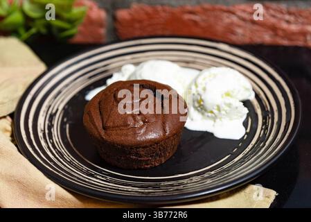 Riche gâteau de lave au chocolat servi chaud avec des boules fondantes de crème glacée à la vanille sur une assiette à dessert noire. Banque D'Images