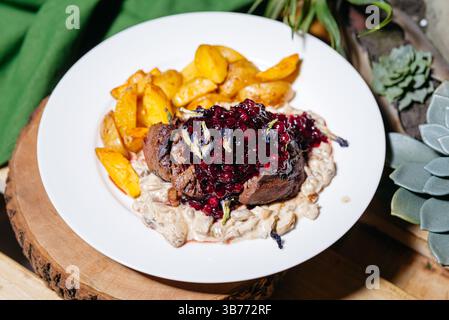 Bifteck rustique de venaison servi avec des pommes de terre dorées rôties, une sauce crémeuse aux champignons et une garniture aux airelles, parfait pour les repas gastronomiques. Banque D'Images