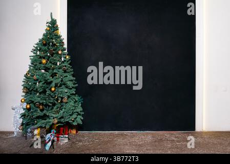 Bel arbre de Noël avec des ornements en or et des cadeaux en dessous, placé dans une pièce minimaliste avec un fond de mur noir. Banque D'Images