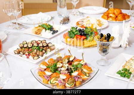 Variété de hors-d'œuvre froids, canapés, olives, fromages et fruits magnifiquement disposés sur une table de banquet formelle pour un événement. Banque D'Images