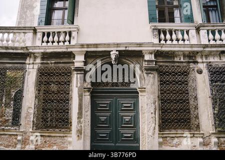Gros plan de la façade d'un bâtiment, dans les rues de Venise, Italie. Porte verte en bois antique. Motifs forgés sur une grille métallique. Balcons avec colu Banque D'Images