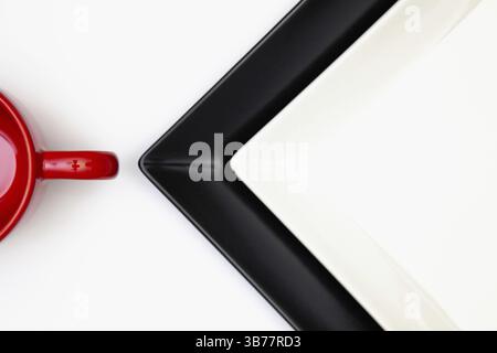 Différentes assiettes noires et blanches et tasse rouge sur la table en bois blanc.vue de dessus. Image à plat Banque D'Images