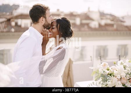 Couple de mariage interracial. Destination mariage beaux-arts à Florence, Italie. Marié caucasien et mariée afro-américaine câlin sur le toit, au soleil Banque D'Images