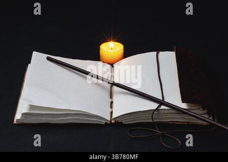 Image de livre magique ouvert, baguette et bougie allumée sur la table dans la pièce sombre Banque D'Images