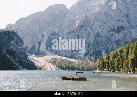 Les jeunes mariés naviguent dans un bateau en bois sur le Lago di Braies en Italie. Mariage en Europe, sur le lac de Braies. Couple de mariage - les rangées de mariés avec des rames en bois, t Banque D'Images
