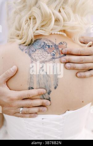 Mariée avec un tatouage Dreamcatcher sur son dos, marié embrasse la mariée et met ses mains sur son dos, gros plan. Banque D'Images