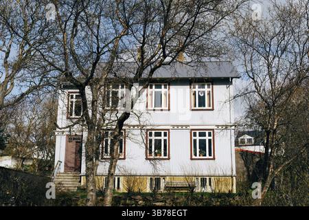Maison bleue classique de deux étages à Reykjavik, la capitale de l'Islande. Arbres de printemps au premier plan. Banque D'Images