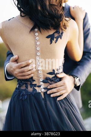 Groom dans un costume bleu embrasse la mariée dans une robe bleue par la taille. Gros plan. Vue arrière. Banque D'Images