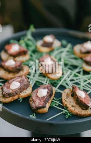 Délicieux canapés de bœuf servis sur du pain grillé garni de légumes verts lors d'un rassemblement chic le soir. Banque D'Images