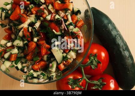 Salade de tomates et de concombre hachées avec oignon rouge, persil, aneth et oignons verts dans un bol en verre, mettant en valeur des légumes frais et colorés prêts pour un h. Banque D'Images