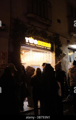 Gelato italienne gros plan en main et scène de shopping au marché nocturne de Rome avec lumières décoratives et foule festive. Photo de haute qualité Banque D'Images