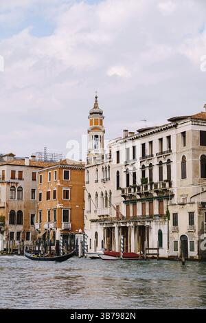 Une gondole avec des touristes navigue le long du Grand canal au milieu des façades de maisons vénitiennes debout sur l'eau à Venise, Italie, Europe Banque D'Images