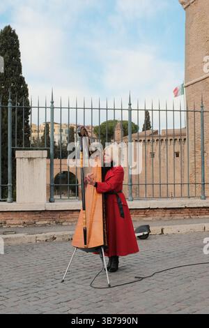 Femme en manteau rouge jouant de la harpe dans une rue pavée près de Castel Sant Angelo à Rome jouant de la musique classique à l'extérieur sous le ciel du jour. Photo de haute qualité Banque D'Images