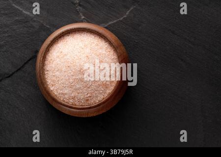Sel rose de l'Himalaya dans un bol en bois - fond de pierre rustique. Banque D'Images