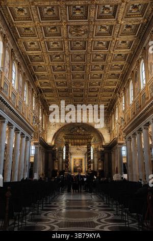 Plafond orné à caissons dorés et intérieur richement décoré de la basilique Sainte-Marie-majeure à Rome Italie avec des rangées de bancs de marbre sol et autel illuminé à l'extrémité éloignée. Photo de haute qualité Banque D'Images