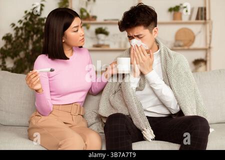 Femme chinoise traitant mari malade donnant des médicaments assis à la maison Banque D'Images