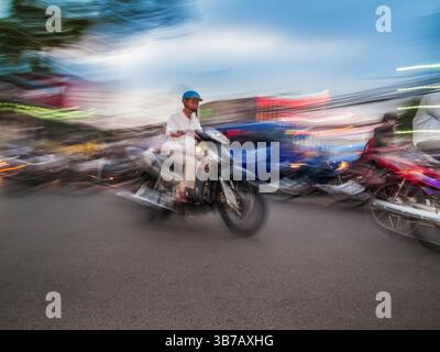 Motos circulant le long d'une route urbaine animée au crépuscule, lumières floues ajoutant de l'énergie à la scène Banque D'Images