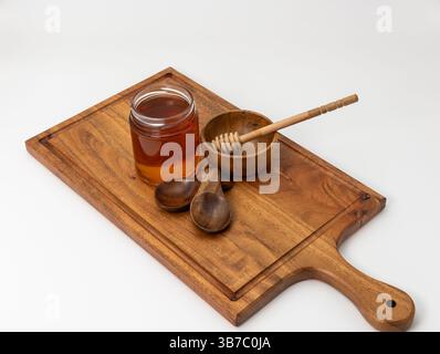Plongeur de miel en bois conservé dans un bol vide avec des cuillères en bois et un pot de miel sur une planche de bois. Banque D'Images