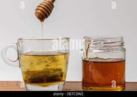 Miel qui coule d'une benne dans une tasse de thé vert conservé à côté d'un pot de miel Banque D'Images