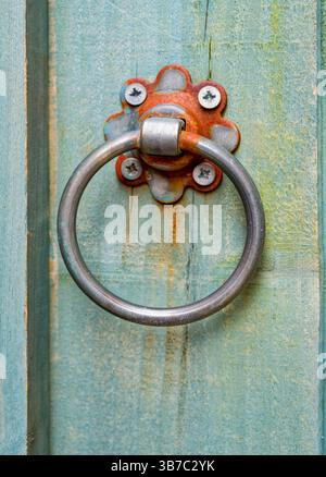 Un anneau en métal légèrement rouillé utilisé comme poignée de porte sur une porte de jardin peinte Banque D'Images