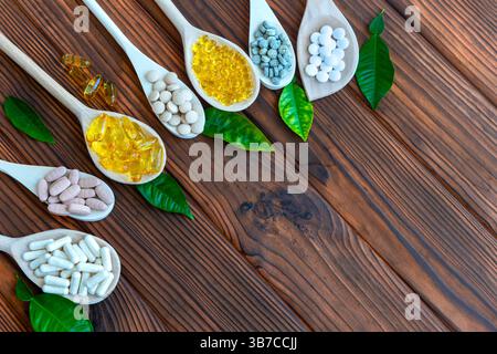 Divers suppléments dans des cuillères en bois avec des feuilles vertes sur fond en bois. Cette image présente plusieurs cuillères en bois remplies de différents types de Banque D'Images