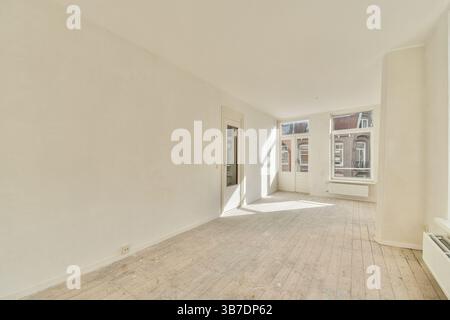 Cette chambre spacieuse et lumineuse dispose de grandes fenêtres qui permettent une abondance de lumière naturelle. La zone a un design minimaliste avec des murs de couleur claire et du parquet. Banque D'Images