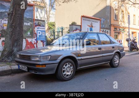 Berline Toyota Corolla argentée classique garée dans une rue de la ville devant des murs urbains colorés et des affiches. Une scène nostalgique de la vie quotidienne dans un Euro Banque D'Images