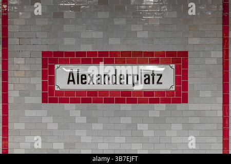 Mur de tuiles avec un panneau de gare « Alexanderplatz » de style vintage dans le U-Bahn de Berlin, encadré par des tuiles rouges et grises, évoquant le design urbain historique. Banque D'Images