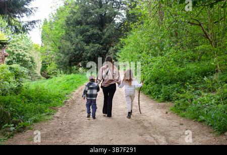 Garçon et fille avec leur mère marchant dans les bois de Stanmer Park sur un sentier au printemps à Brighton, Royaume-Uni Banque D'Images