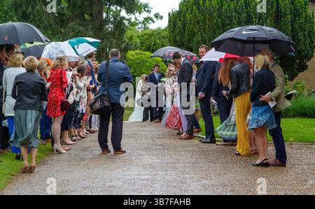 Un mariage traditionnel de l'église britannique sous la pluie avec des parapluies. Ensuite, les invités font la queue pour former une allée et jettent des confettis au couple. Banque D'Images